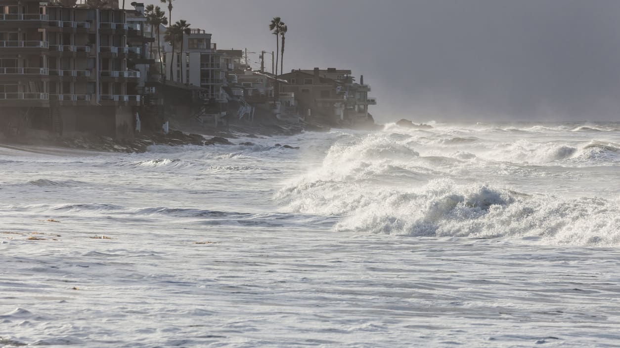 A large wave crashes into a building on the beach.