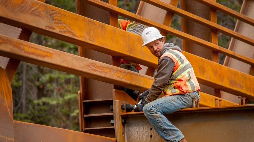 A construction worker is working on a rusty metal bridge.