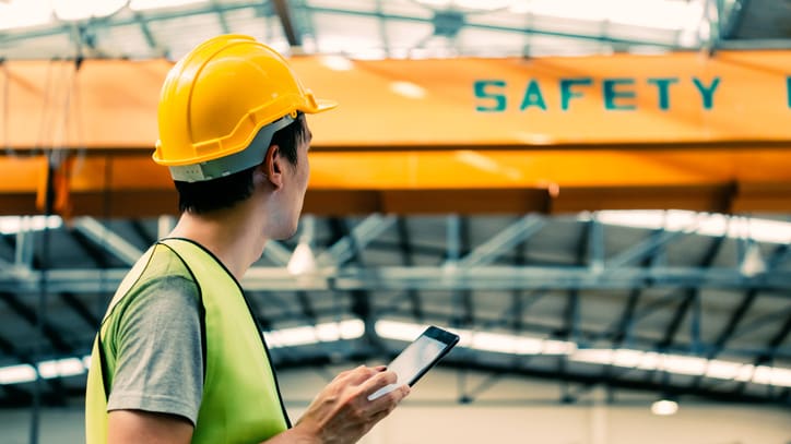 A man wearing a hard hat and safety vest is looking at his phone.