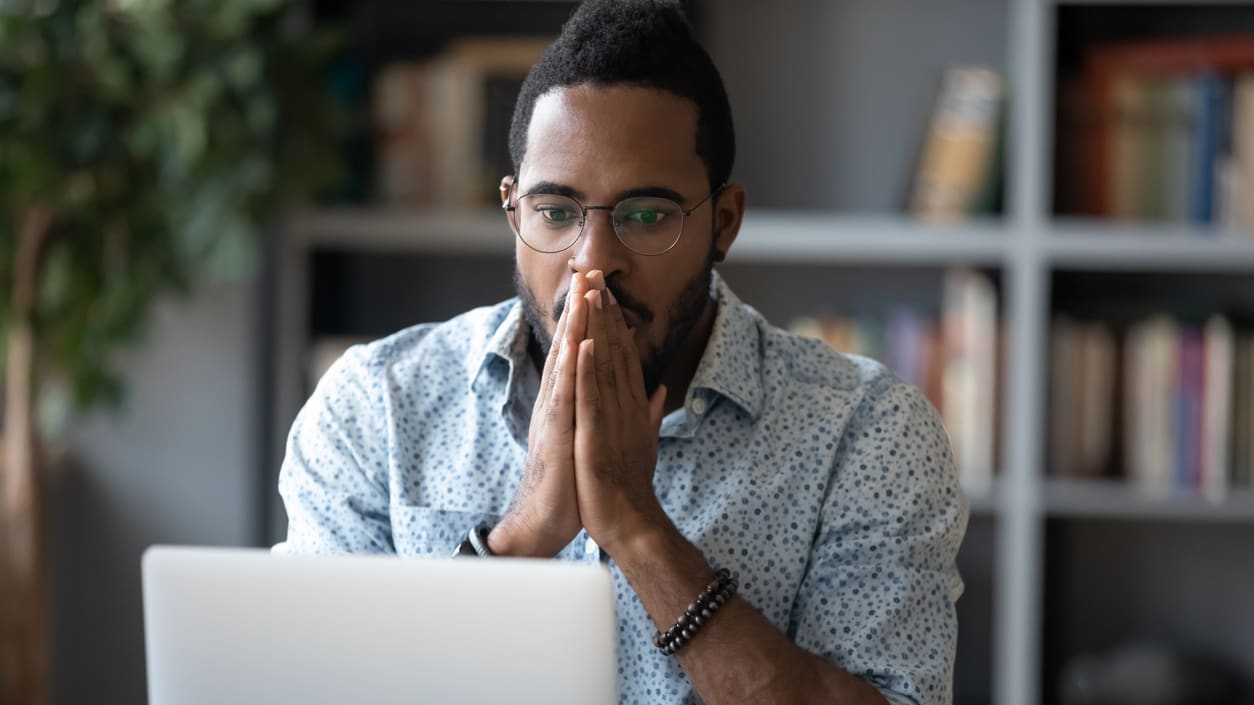 A man with his hands on his face in front of a laptop.