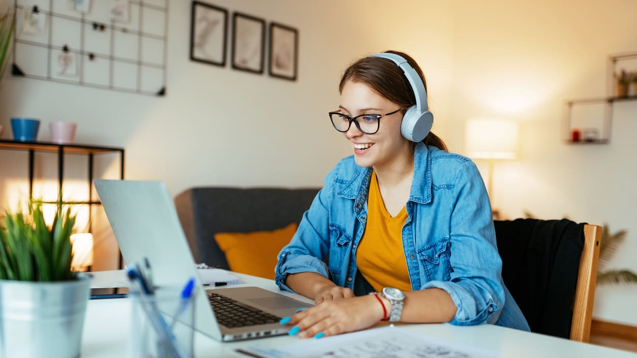 A young woman wearing headphones is working on her laptop at home.