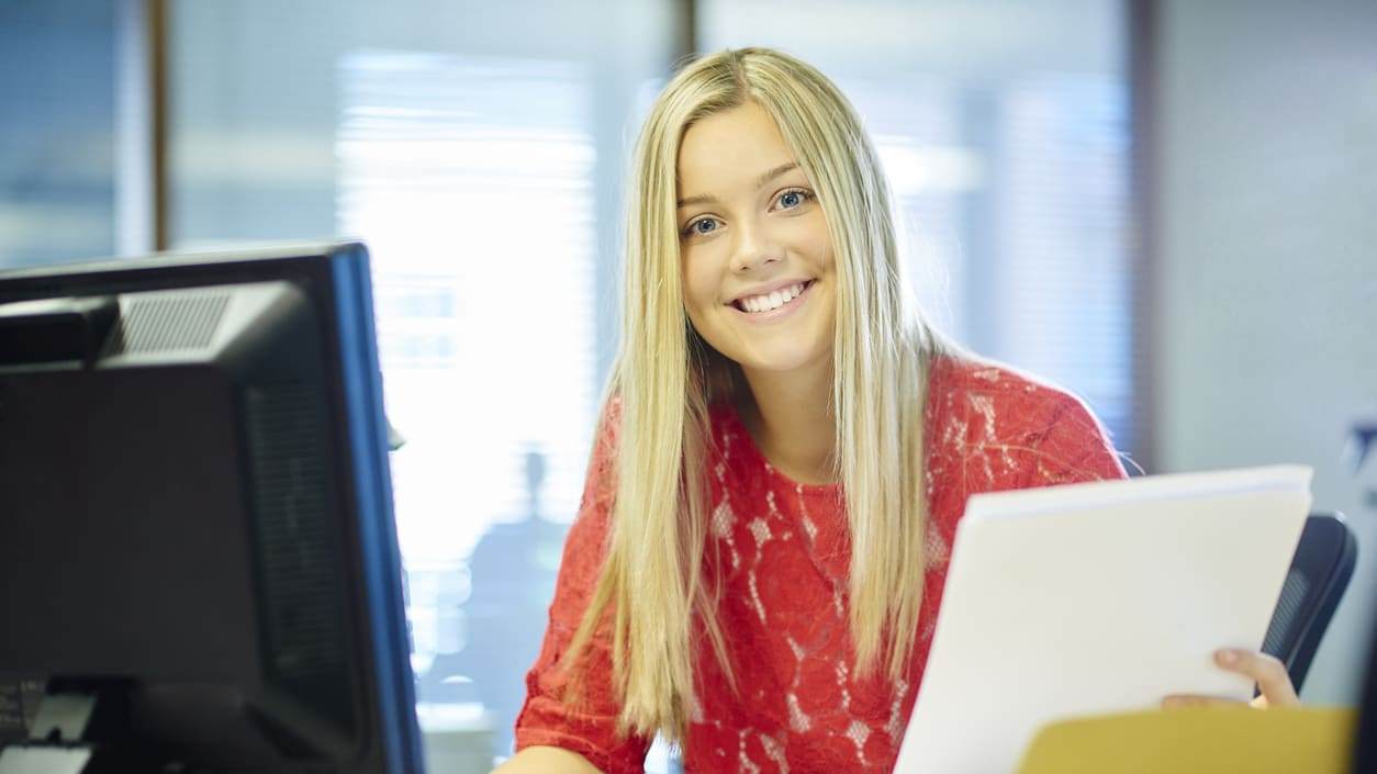 A smiling woman sitting at a desk in front of a computer.