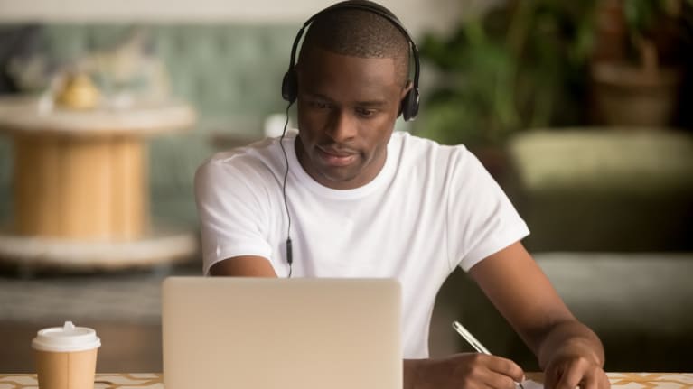 A man wearing a headset and writing on a laptop.