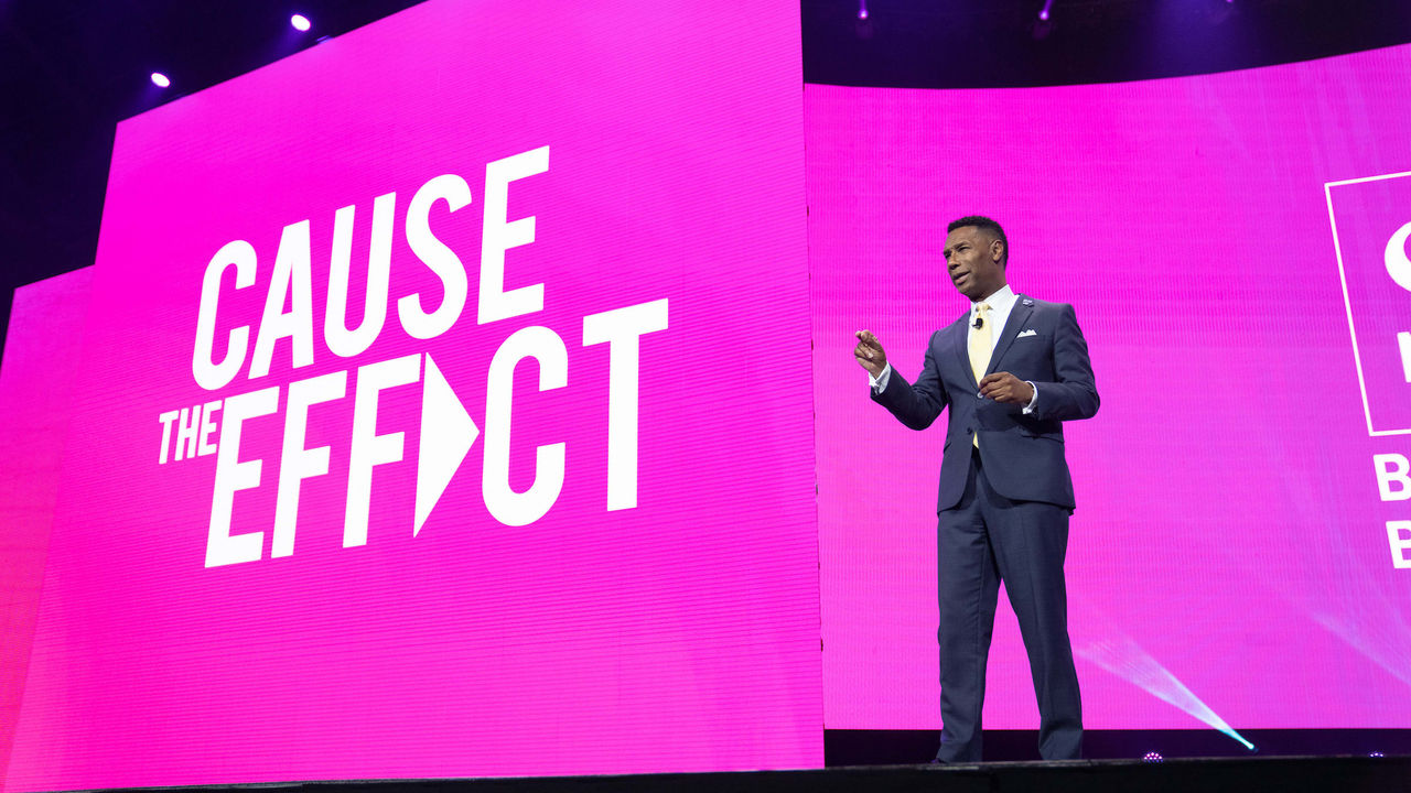Johnny C. Taylor Jr. standing on stage in front of a pink screen that says cause the effect.