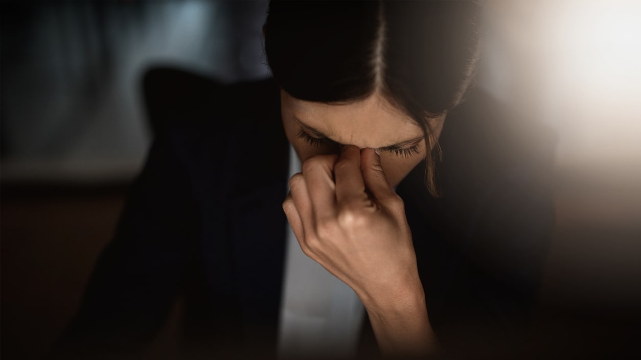 A woman in a business suit is holding her face in the dark.