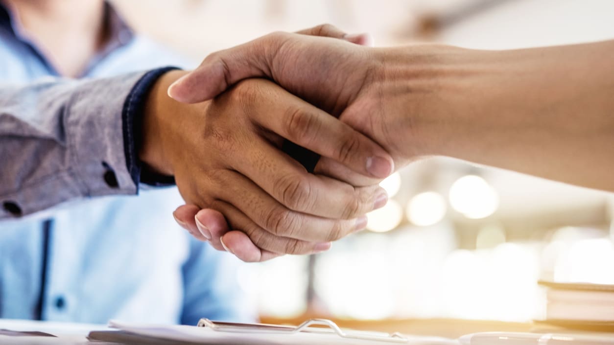 Two business people shaking hands in front of a desk.