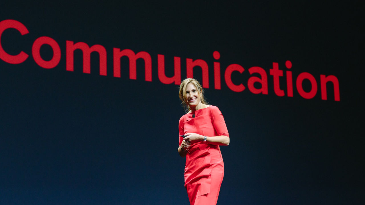 A woman in a red dress standing on stage with the word communication.