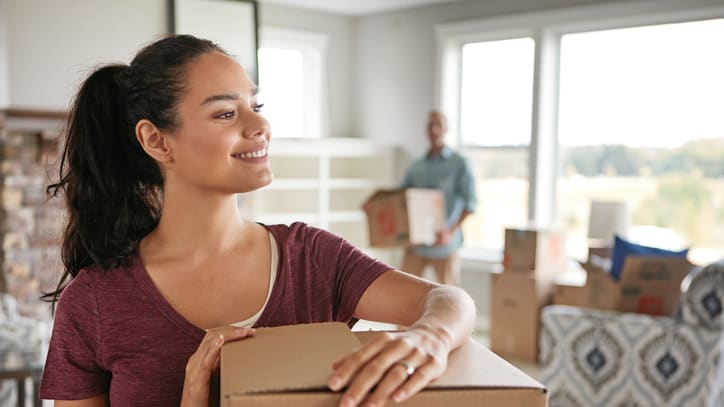 A woman holding a moving box in front of a living room.