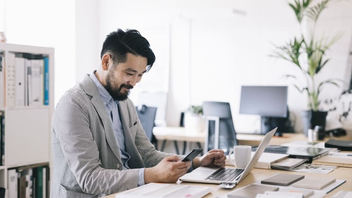 A businessman using a laptop and cell phone in an office.