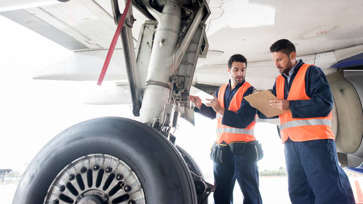 Two men standing next to an airplane with a clipboard.