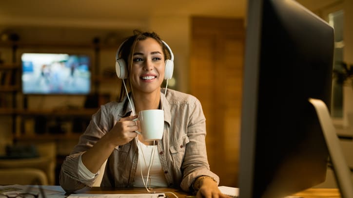 A woman wearing headphones is sitting at a desk with a cup of coffee.