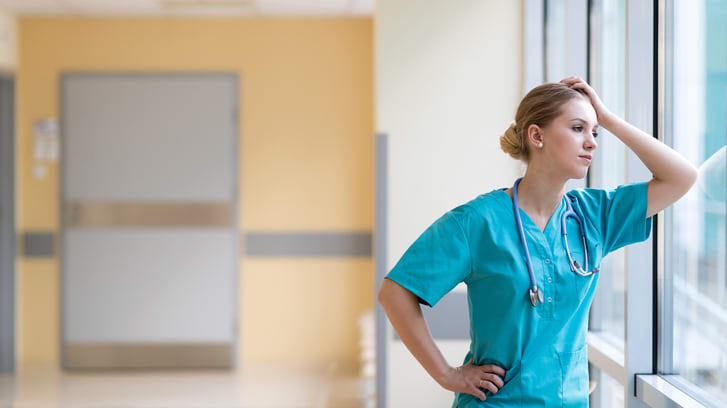 A nurse standing by a window in a hospital hallway.
