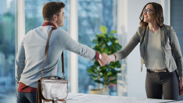 A man and woman shaking hands in an office.