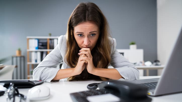 A woman is sitting at a desk with her hands on her face.