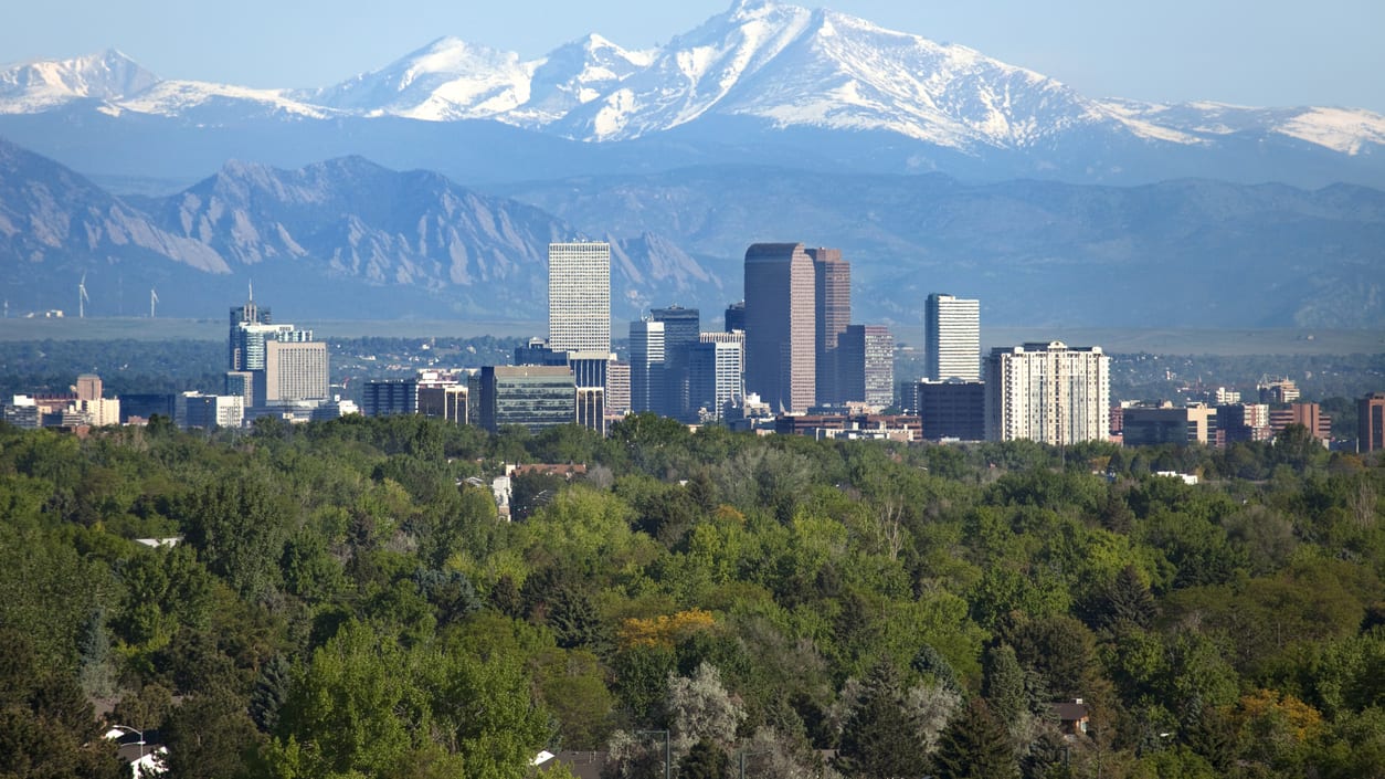 A view of the city of denver with snow capped mountains in the background.