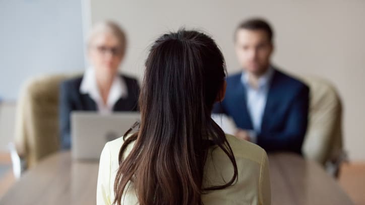 A woman is sitting at a table in front of a group of people.