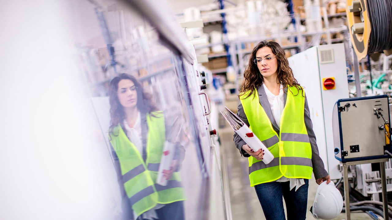 A woman in a safety vest walking through a factory.
