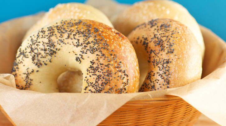 Bagels with sesame seeds in a basket on a wooden table.