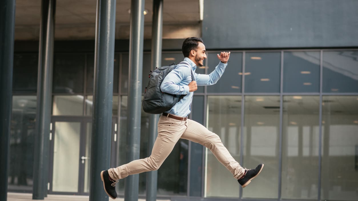 A young man jumping with a backpack in front of a building.