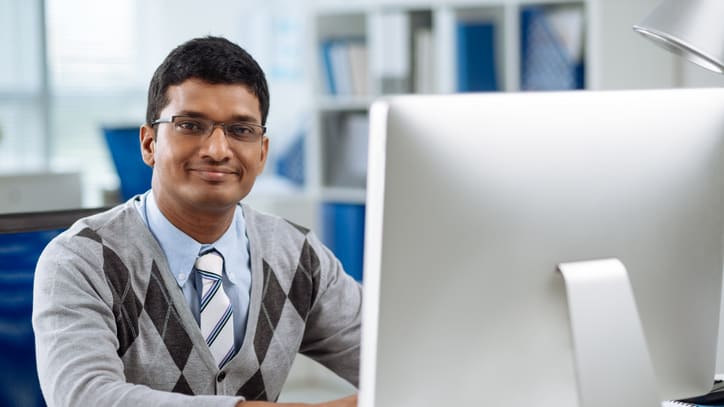 An indian man sitting in front of a computer.