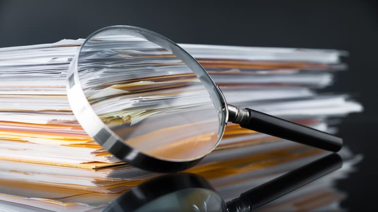 A magnifying glass on top of a stack of documents.