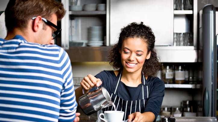 A woman is pouring a cup of coffee for a man at a coffee shop.