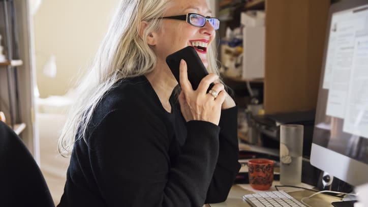 A woman talking on a cell phone in front of a computer.