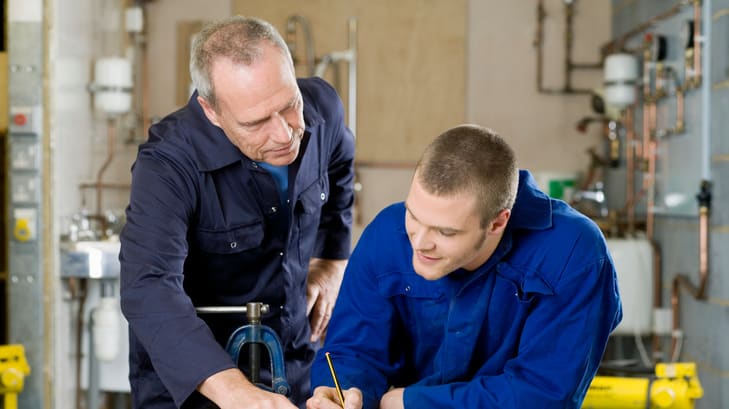 Two plumbers working together in a workshop.