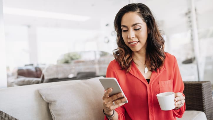 A woman sitting on a couch with a cup of coffee and a smart phone.