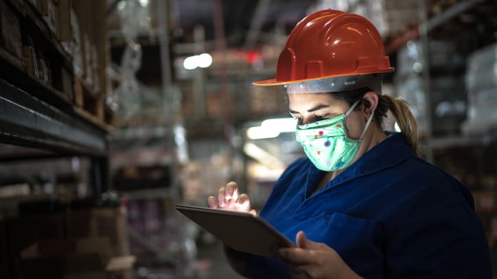 A woman wearing a hard hat is using a tablet in a warehouse.
