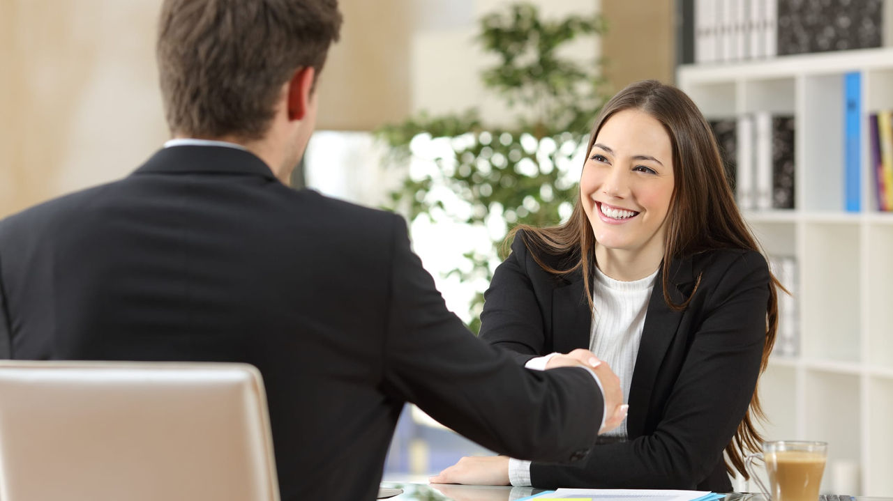 A business woman shaking hands with a man in an office.