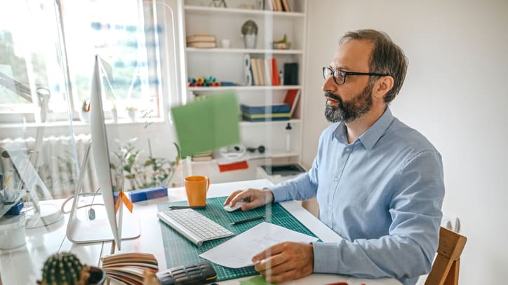 A bearded man working at a desk in his home office.