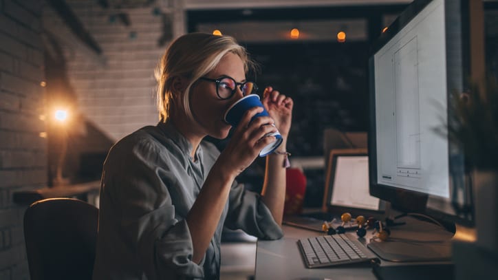 A woman drinking coffee in front of a computer.