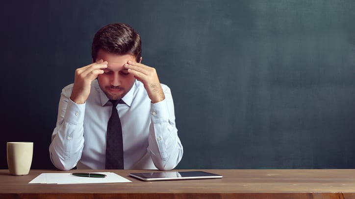 A businessman is sitting at a table with his hands on his head.