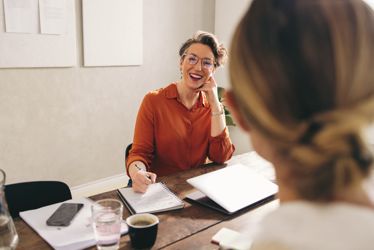 Female hiring manager smiling happily while interviewing a job candidate in her office. Cheerful businesswoman having a meeting with a shortlisted job applicant in a modern workplace.