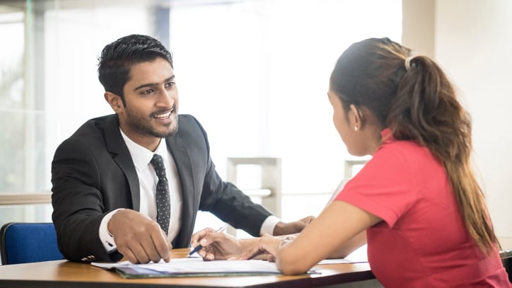 A man and woman talking at a desk in an office.