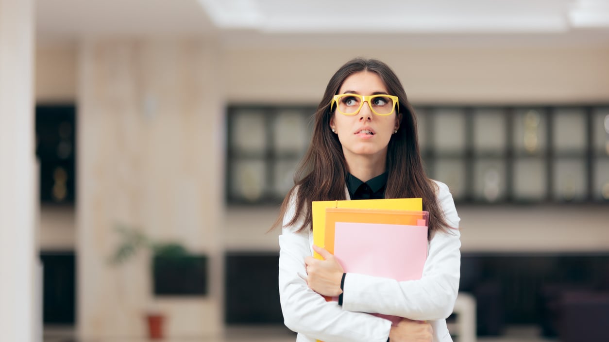 A woman in glasses holding a folder in an office.