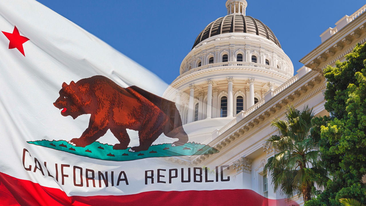 The california state flag is flying in front of the capitol building.