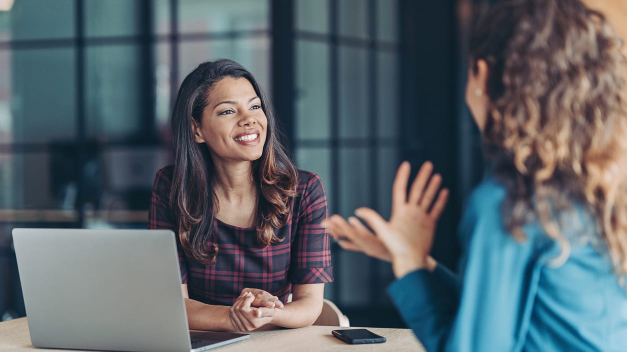 Two women talking at a table in an office.