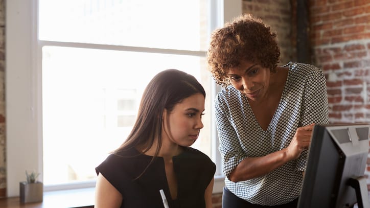 Two women working on a computer in an office.