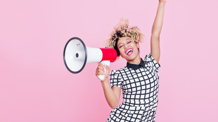 A young woman holding a megaphone over pink background.