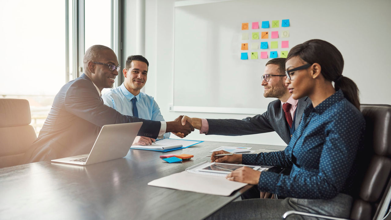 A group of business people shaking hands at a conference table.