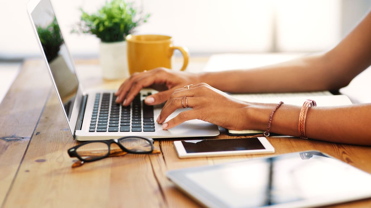 A woman typing on a laptop on a wooden table.