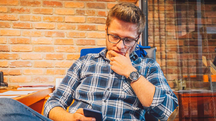 A man sitting in an office chair looking at his phone.