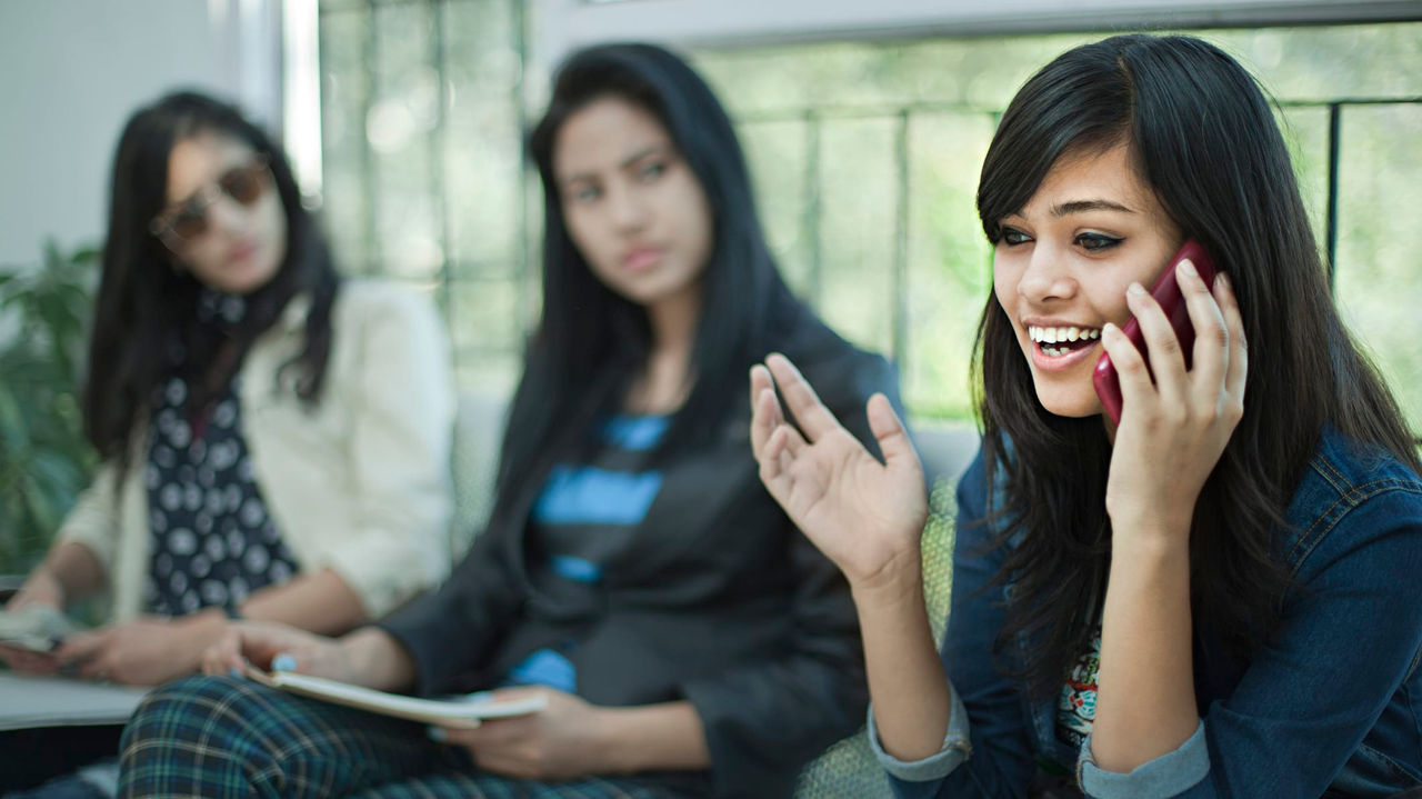 A group of girls sitting on a bench talking on their cell phones.