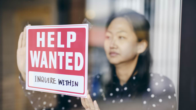A woman holding up a sign that says help wanted.