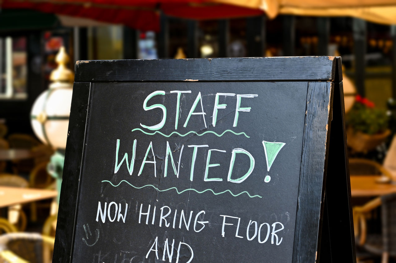 Sign outside restaurant reading Staff Wanted Now Hiring 