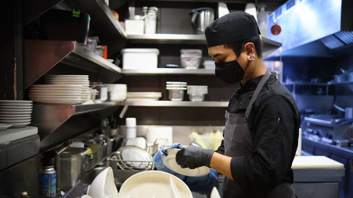 A chef wearing a mask is preparing dishes in a kitchen.