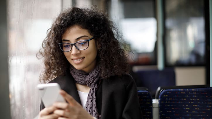 A young woman looking at her phone while sitting on a train.