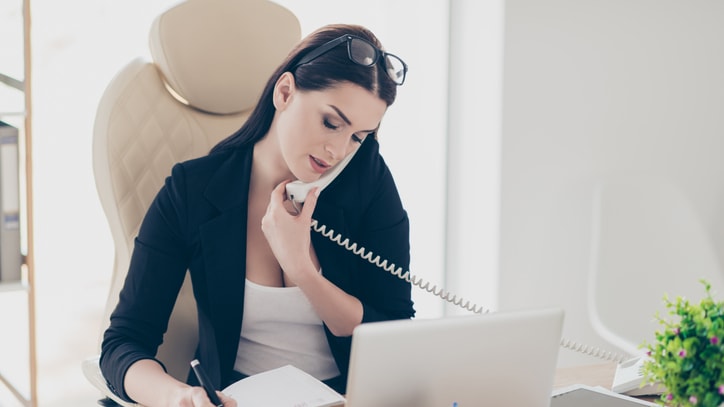 A woman is talking on the phone while sitting at her desk.